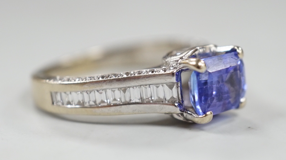 A modern 18ct gold and single stone emerald cut tanzanite set dress ring, with graduated baguette and round cut diamond set shoulders and graduated baguette cut diamond set heart shaped setting, size I, gross weight 4.7